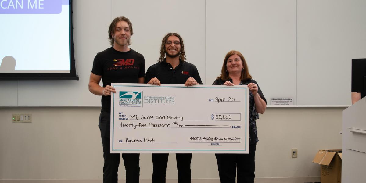 Two Business Pitch winners holding an oversized check with Stephanie Goldenberg.