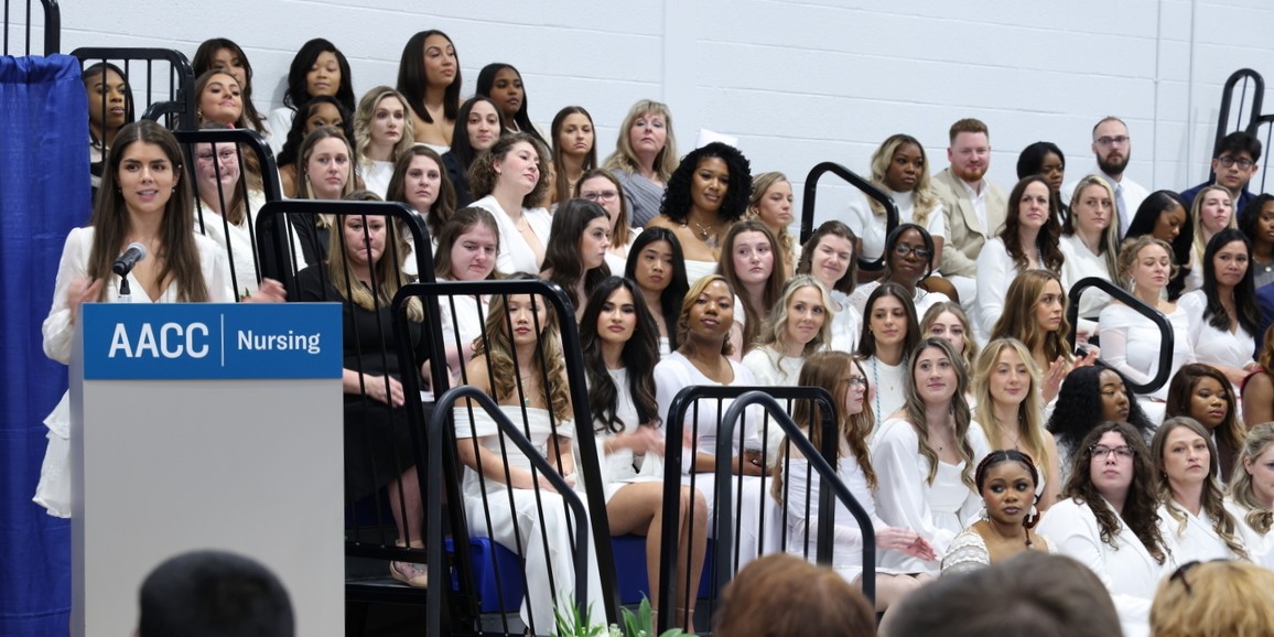 A speaker at the podium as a group of nursing grads listen.