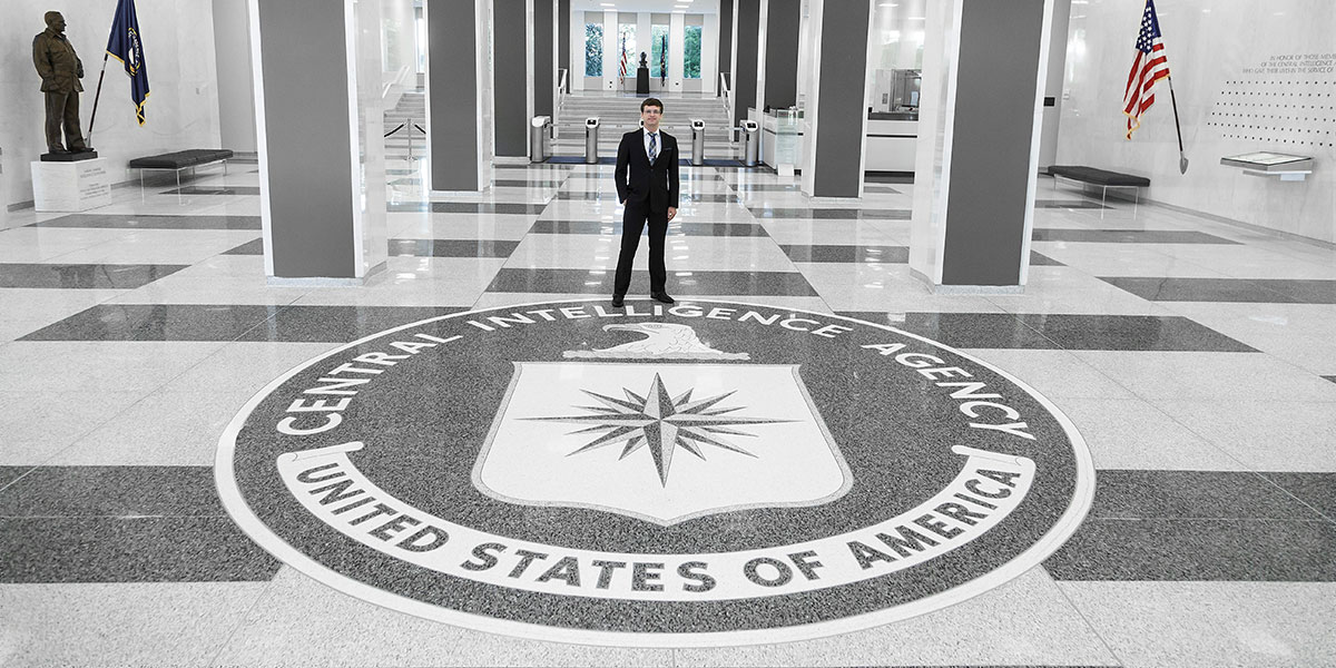 Adam Hertz stands in a building behind the Central Intelligence Agency logo