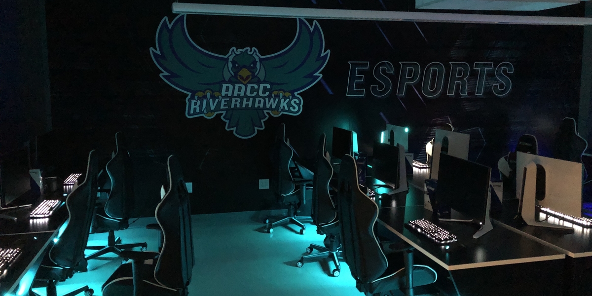 Image of AACC Riverhawks logo with Esports written on the wall. Image of gaming chairs with computers lined in a row.