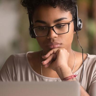 Student studies her laptop while wearing headphones.