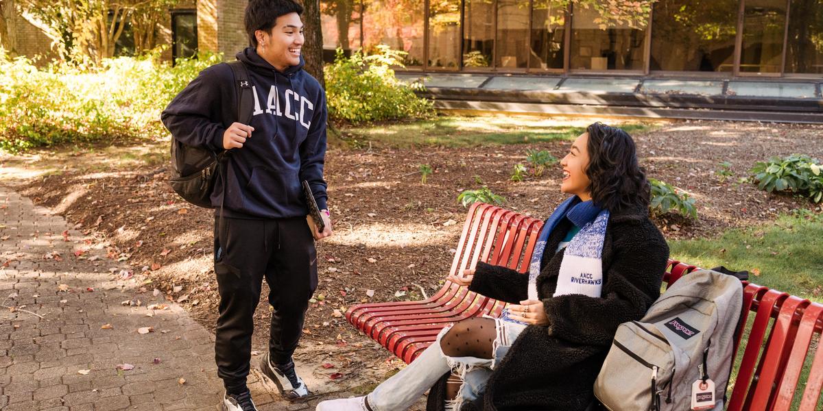 One student standing and talking to student at bench.