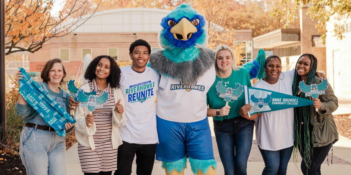 A group of students posing with AACC mascot, Swoop, while holding AACC gear.