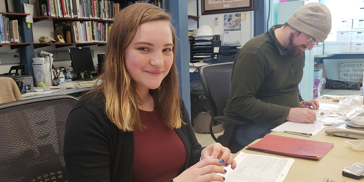 Archaeology Intern Gabrielle Rapine looking at artifacts.