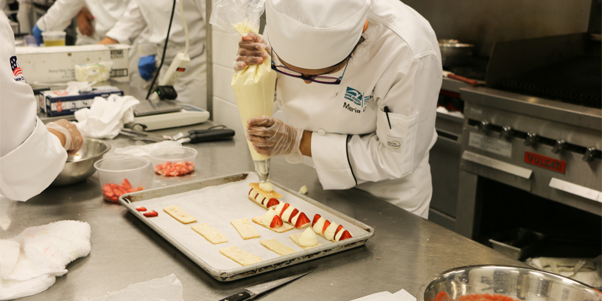 An HCAT student pipes cream filling into her desserts.