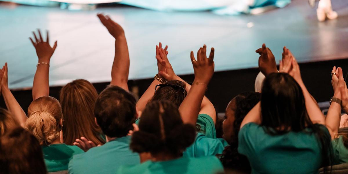 People in an auditorium clapping and cheering as seen from behind.