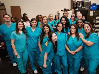 C.E.W.D. graduates in teal scrubs posing together.