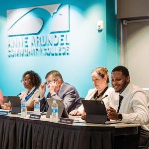 Keshawn Johnson sitting at a table and smiling during a Board of Trustees meeting.