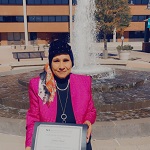 Fatma Ebaid holding a certificate in front of the fountain at Glen Burnie Town Center.
