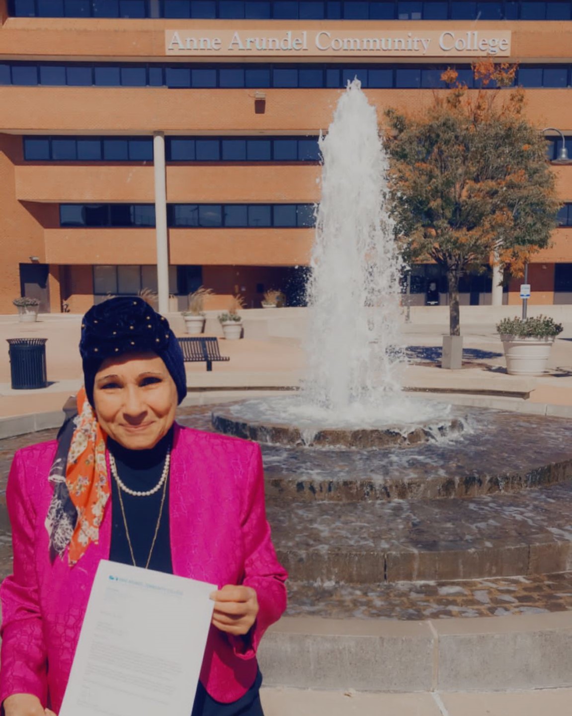 Fatma Ebaid holding a certificate of completion in front of the fountain at AACC Glen Burnie Town Center.