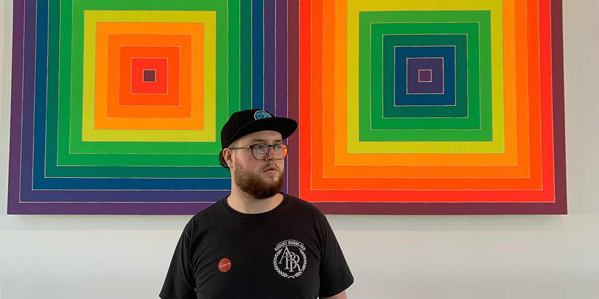 James in front of a colorful, geometric art piece. He is looking into the distance.
