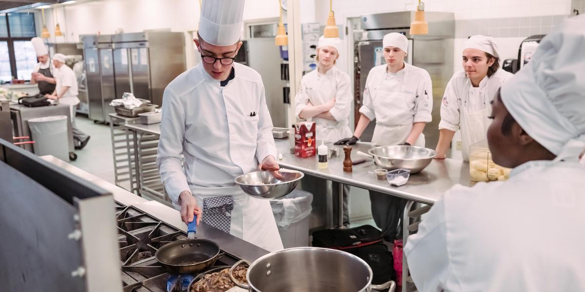 Students watch as a guest chef places meat into a skillet.