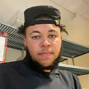 Zack looking at the camera in a kitchen and culinary uniform.