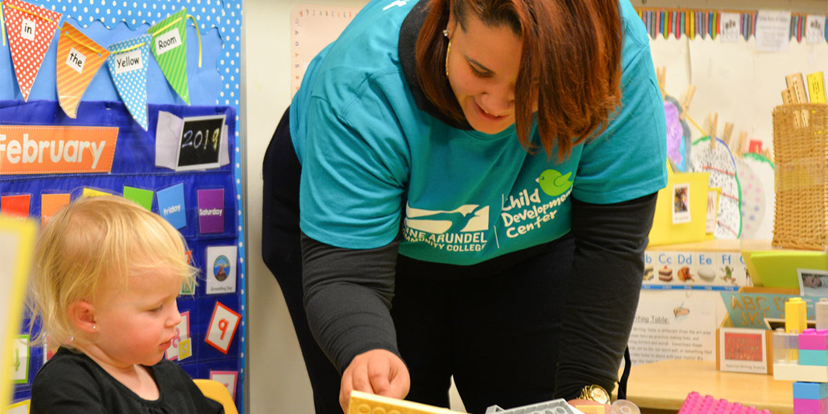 A child care provider helps toddler.