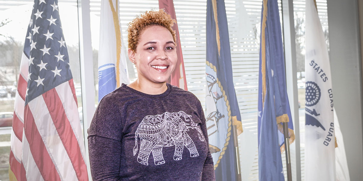 Shanelle Jones stands in front of the U.S. and armed forces flags.