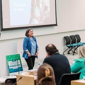 A student stands before a crowd in a classroom presenting her business pitch