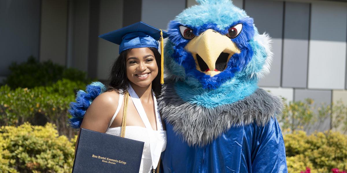 AACC grad posing with AACC mascot, Swoop