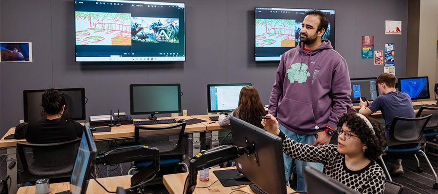 A student points to a screen with an instructor standing nearby in a game design class.