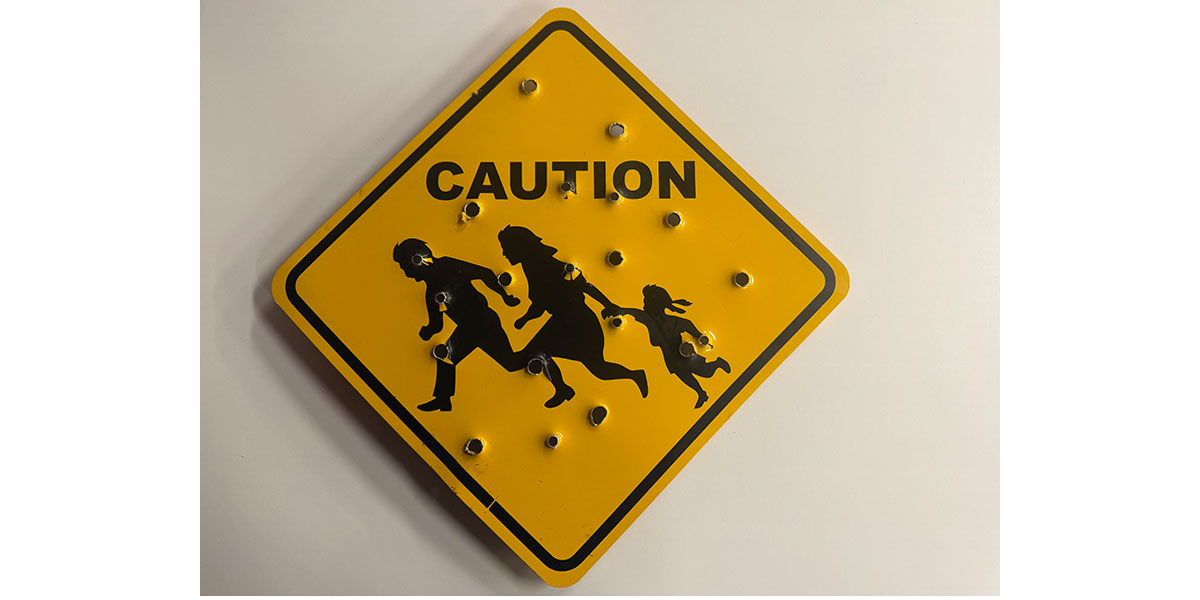 A yellow school crossing sign with two adults and child riddled with holes.
