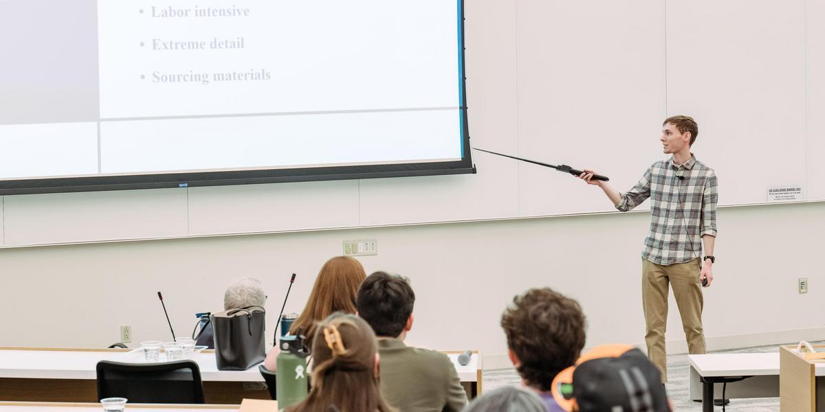 A student uses a pointing stick to point to a screen showing a slideshow.