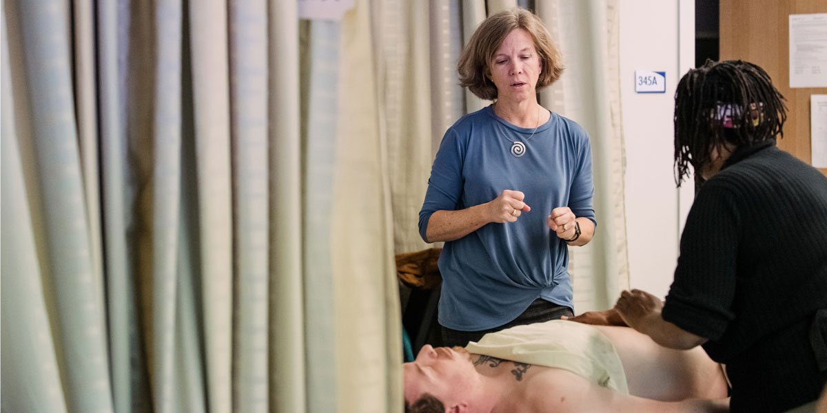Instructor performing hands-on instruction in front of student in massage therapy class.
