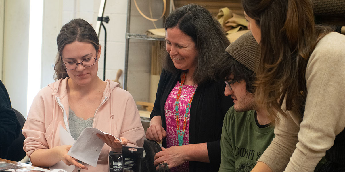 Students in an anthropology class work on an art project as their professor looks on.