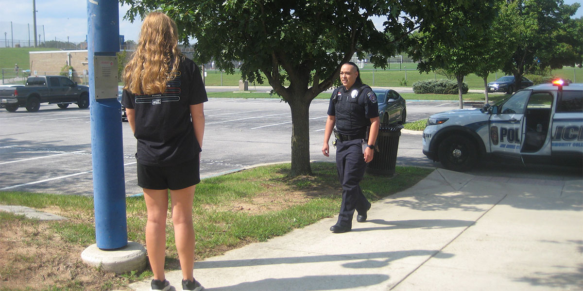 A Public Safety officer interacts with a student standing on a sidewalk.