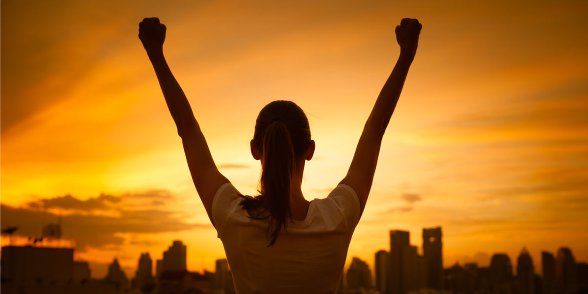 Woman with arms raised at sunrise.