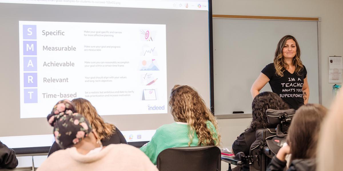 A TEACH instructor standing in front of a classroom with a screen behind her.