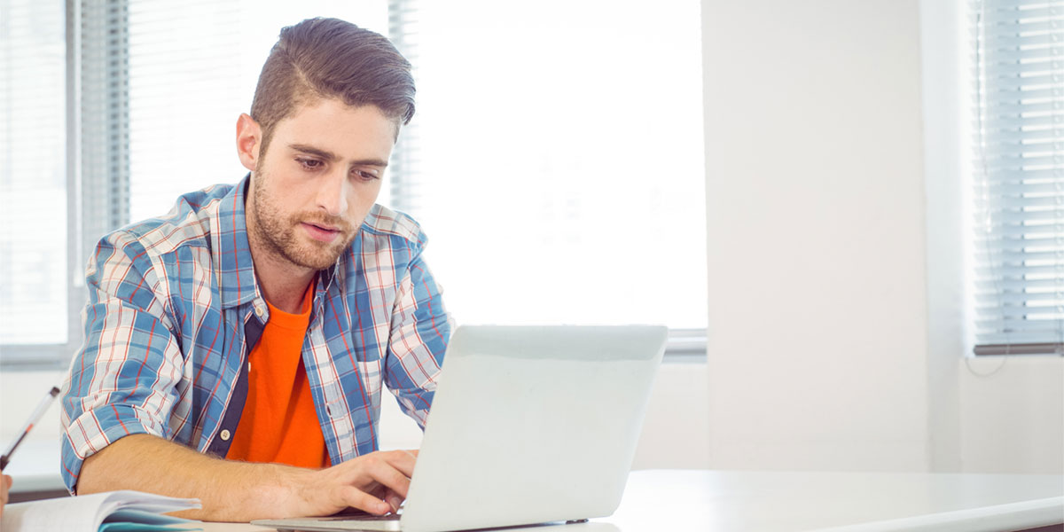 Male student sitting at a table with laptop computer.