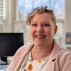 Headshot of KT Perkins with computer and window behind them