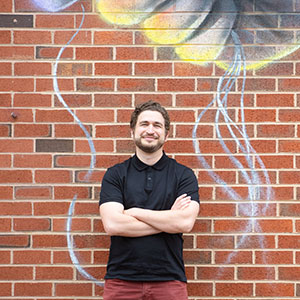 Owen Silverman Andrews leaning against a brick wall covered in art