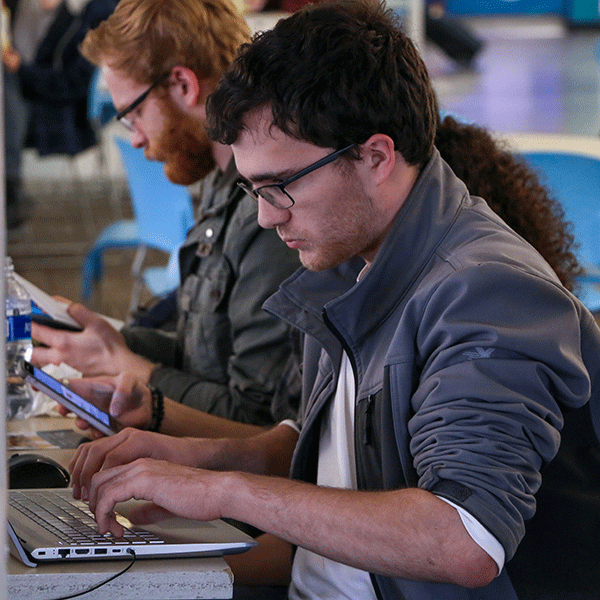 Student typing onto a laptop. Other students in the background.