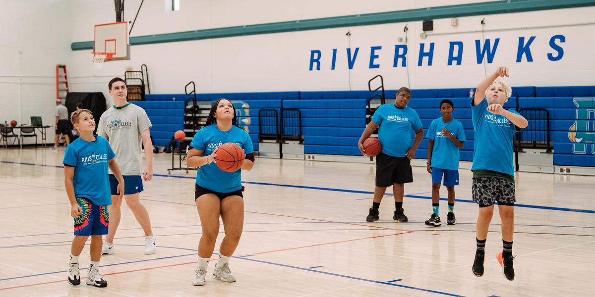 A group of students shoots basketballs in a gymnasium.