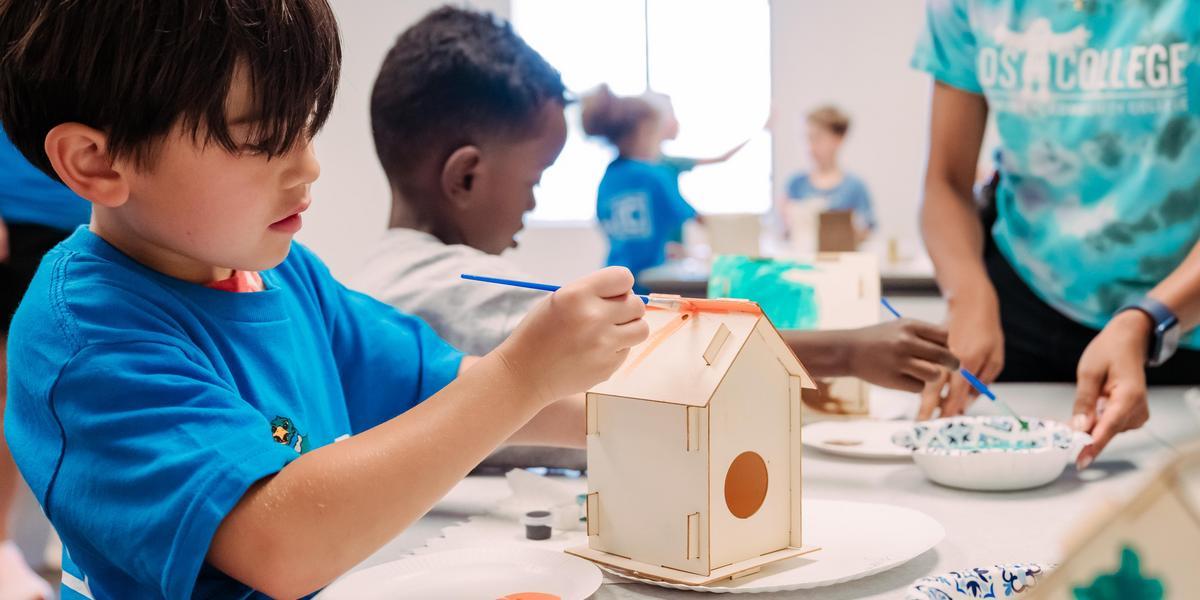A student paints a wooden birdhouse.