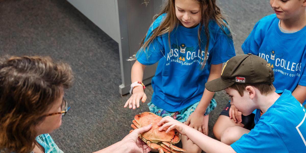 A group of students touch a crab being held by an adult.