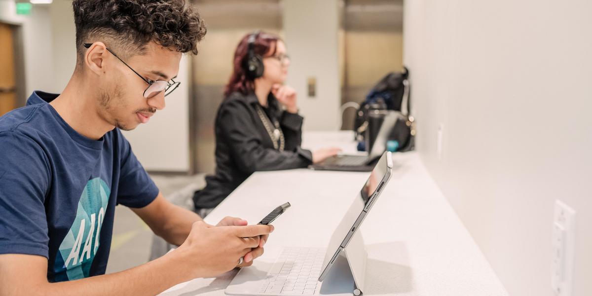 Student on cell phone with tablet in front of them.