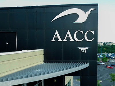 A drone flying in front of a building with AACC logo on it